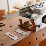 Professional jointer with collection of metal knives placed on wooden table in workshop with special metal machines on blurred background