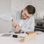Man wearing glasses using a screwdriver to fix a device on a kitchen table.