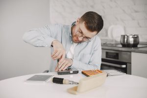 Man wearing glasses using a screwdriver to fix a device on a kitchen table.