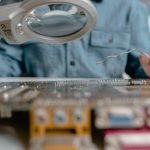 A detailed view of electronic circuit inspection using a magnifying glass and tools.
